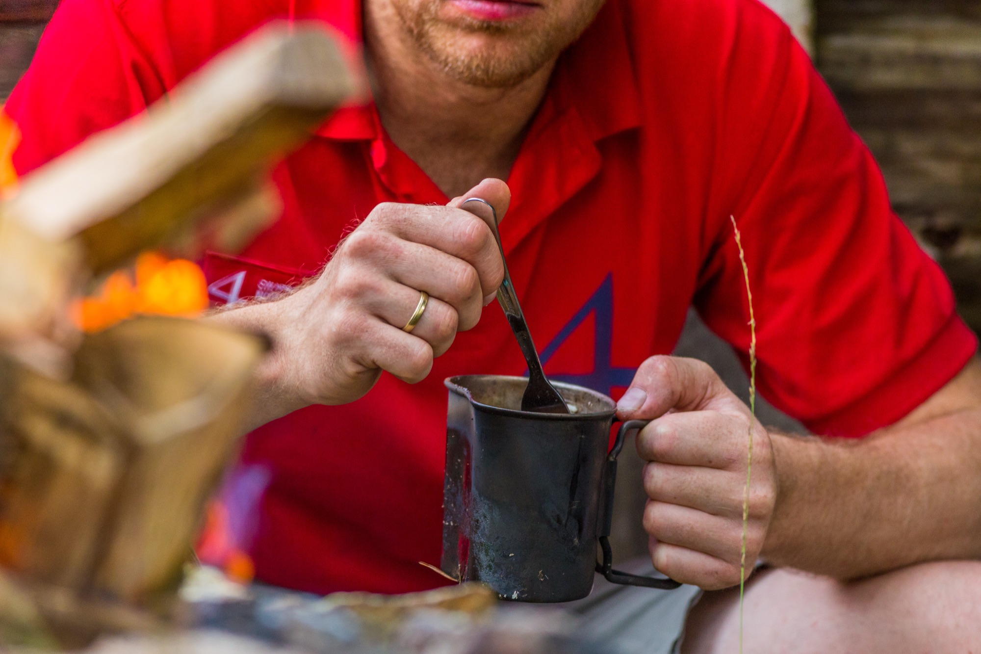 Man i 4M-tröja rör i kaffe vid elden